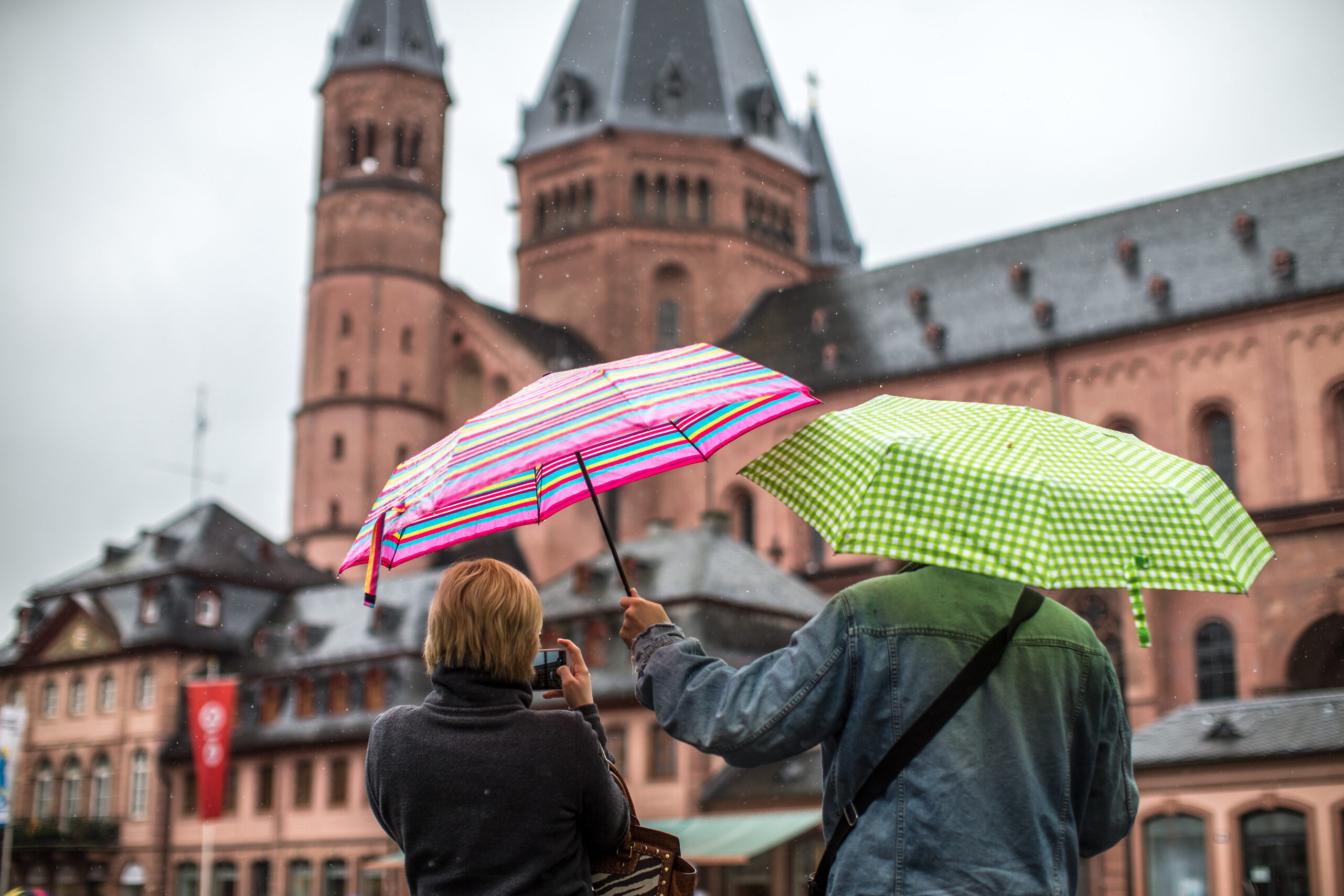 Zwei Menschen mit Regenschirmen, vor dem Mainzer Dom