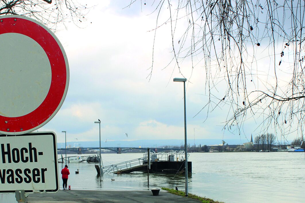 Ein Hinweisschild am überfluteten Rheinufer.