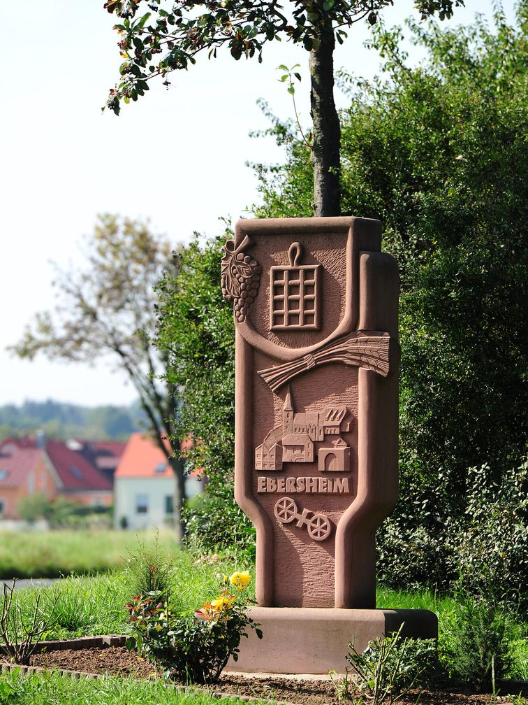 Steindenkmal mit der Inschrift "Ebersheim", einer kleinen Stadtansicht, dem Mainzer Rad und weiteren kleinen Symbolen